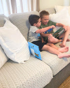 Kids sitting and playing on a textured light grey couch.