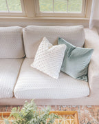 Light gray sofa with textured pillows in a room with a window and rug.