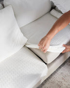 Person adjusting a white sofa cover on   a light gray sofa.